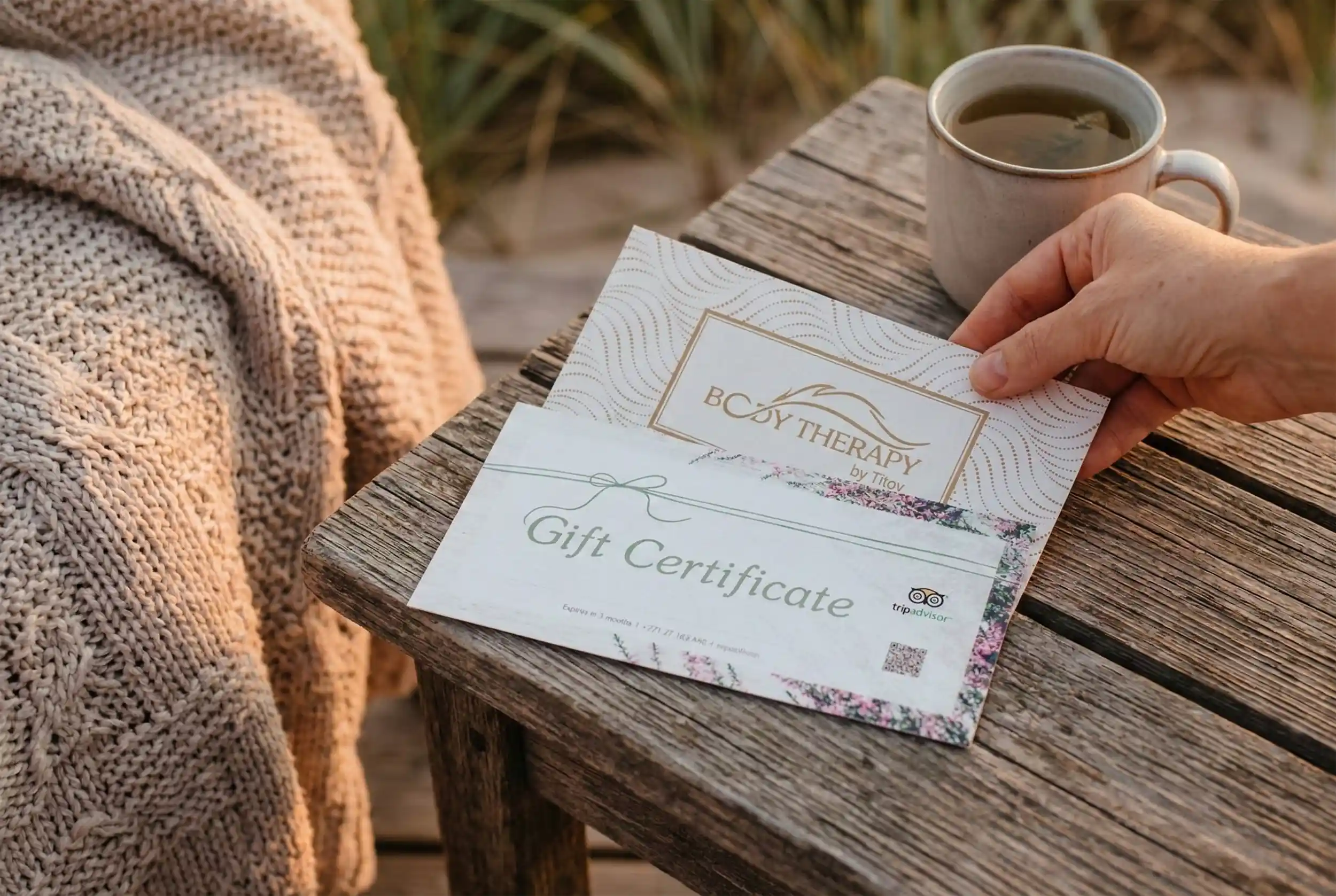 Подарочные карты Therapy by Titov на деревянном столе рядом с лавандой, кружкой травяного чая и мягким пледом.